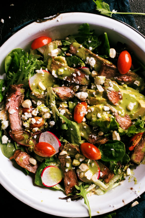 A seared steak salad topped with a fresh cilantro lime vinaigrette topped with fire roasted corn, ripe cherry tomatoes and radishes.